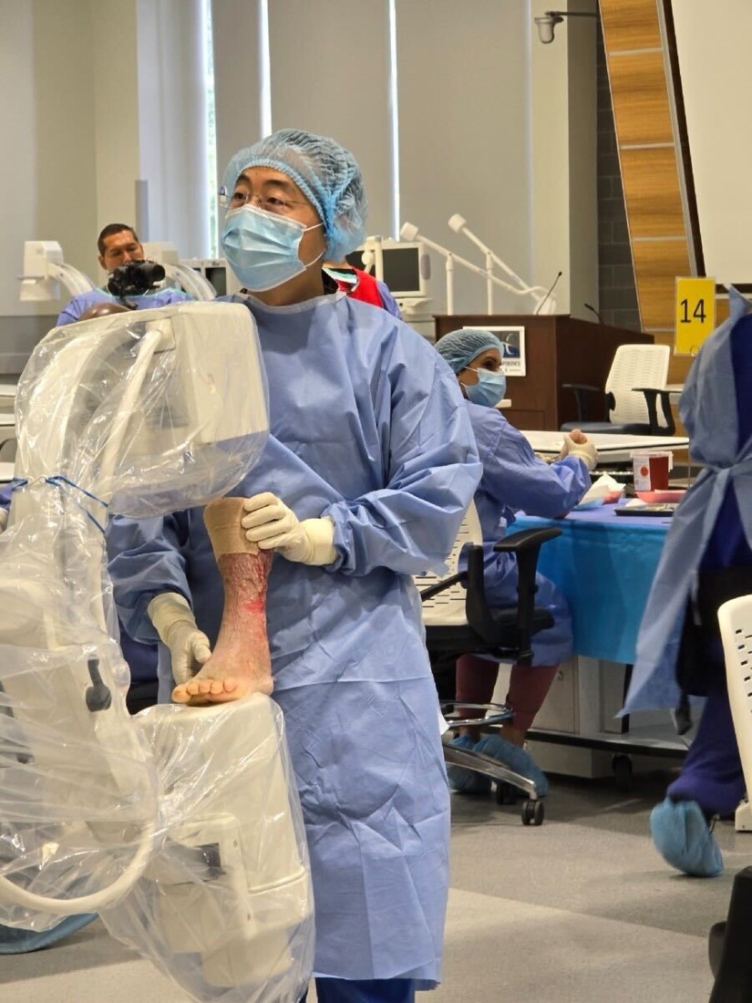 Dr. TJ Ahn in full surgical attire teaching at a cadaver lab, C-arm at his side